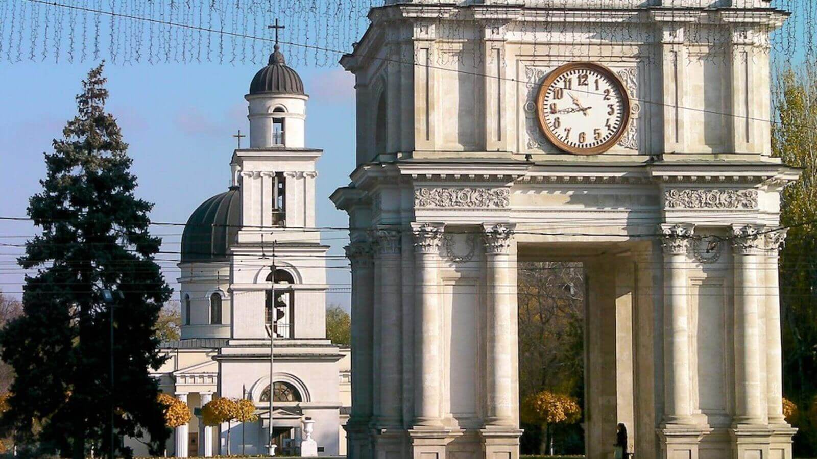 Chișinău's Arcul de Triumf framed by central-park trees with the Cathedral spire beyond.