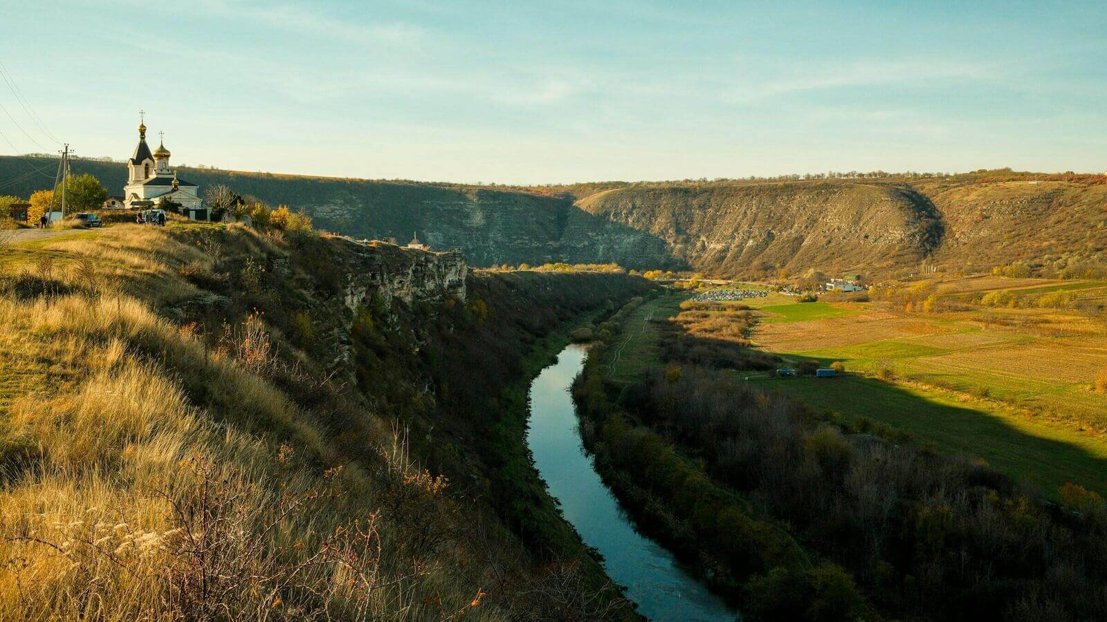 Forested river bend with a small whitewashed church on a hilltop — central Moldova landscape evocative of Old Orhei.