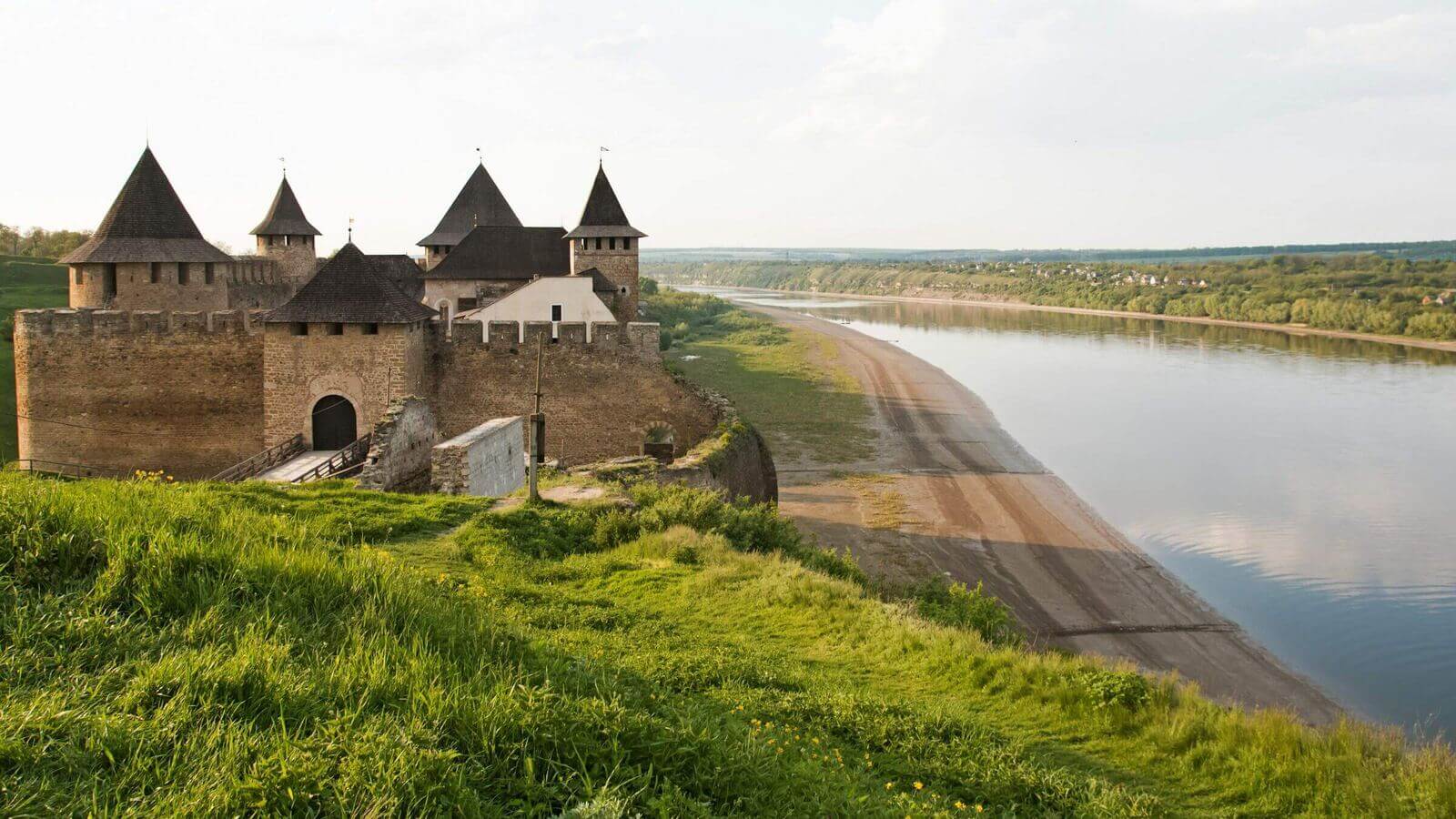 Stone-walled medieval fortress on a green hill above the Dniester river valley.